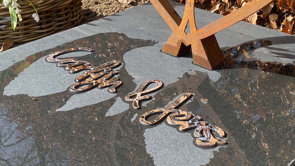 Gepolijste RVS letters op een liggende grafsteen van zwart graniet